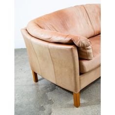 a tan leather chair with wooden legs and arm rests on the concrete floor in front of a white wall