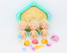 three dolls are standing in front of a doll house with toys around them on a white surface