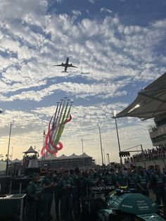 a group of people standing in front of an air plane flying over the sky with colorful kites