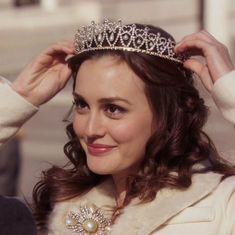 a woman wearing a tiara and smiling at the camera while holding her hair in one hand