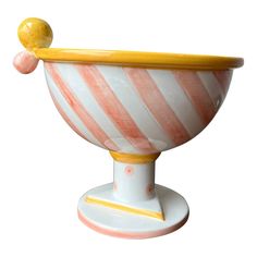 a white and orange striped bowl with a yellow top on a stand against a white background