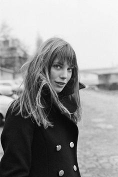 a black and white photo of a woman with long hair wearing a peal coat