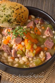 a bowl of ham and bean soup next to a piece of bread on a table