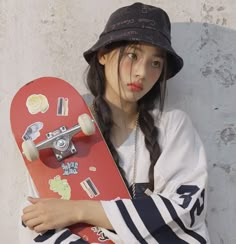 a young woman holding a skateboard with stickers on it's side and wearing a hat