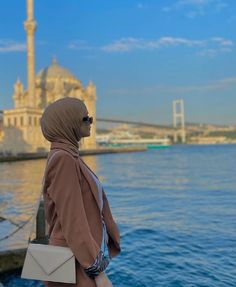 a woman wearing a headscarf looking out over the water in front of a large building