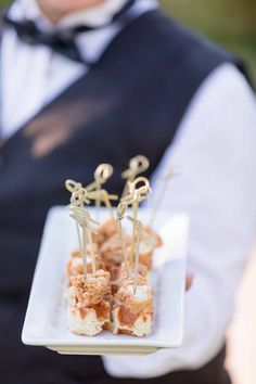 a man in a vest holding a plate with food on it and two small sticks sticking out of the top