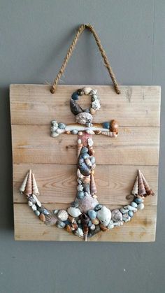 an anchor made out of seashells hangs on a wooden plaque with rope and hooks