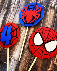 three spiderman cupcake toppers are on a wooden table, one is blue and the other is red