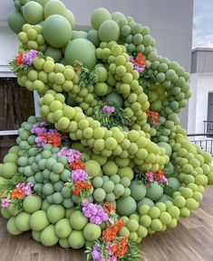 a sculpture made out of green balls and flowers on a wooden floor in front of a building