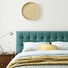 a bed with a blue headboard and yellow pillows in a white room next to a lamp