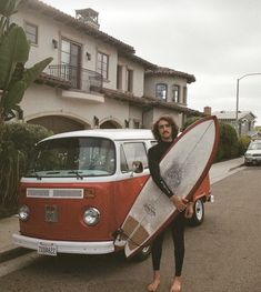 a woman holding a surfboard in front of a vw bus on the street