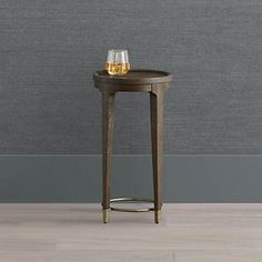 a small wooden table with a glass on it next to a gray wall and hardwood floor