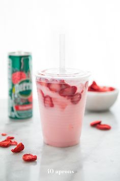 a drink in a plastic cup with strawberries on the side and a can of soda behind it