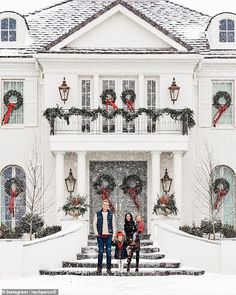 a family standing in front of a large white house with christmas wreaths on it