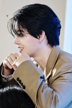 a woman with black hair is smiling and looking to the side while wearing a tan jacket