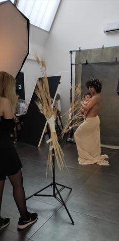 a woman sitting on a chair in front of a camera and another person standing next to her