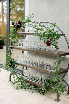 an assortment of wine glasses and greenery are arranged on a metal shelf in front of a window