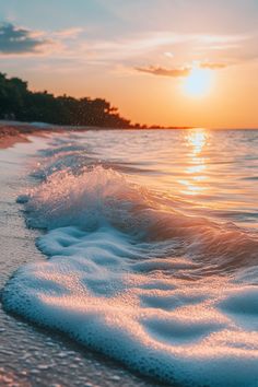 the sun is setting over the water and waves on the beach, as seen from the shore