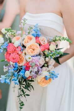 a woman in a white dress holding a bouquet of pink, orange and blue flowers