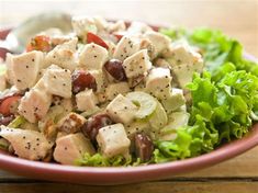 a salad with chicken, olives and lettuce in a red bowl on a wooden table