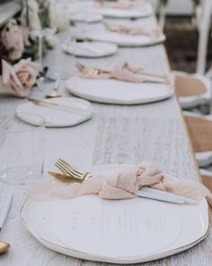 the table is set with white plates and pink napkins, gold cutlery and silverware