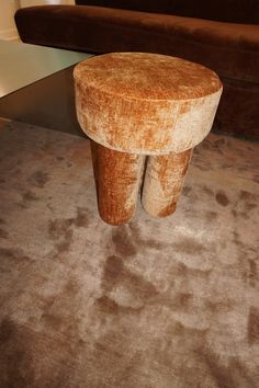 a small stool sitting on top of a carpeted floor next to a brown couch