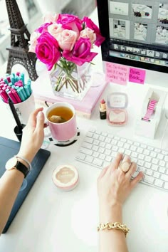 a person sitting at a desk with a keyboard, mouse and pink flowers in a vase