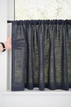 a hand is holding the curtain in front of an open window with black curtains on it