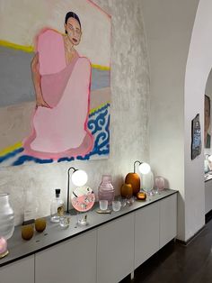 a large painting hangs on the wall above a buffet table with vases and lamps