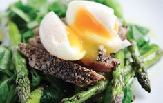 a white plate topped with asparagus and an egg on top of some sort of meat