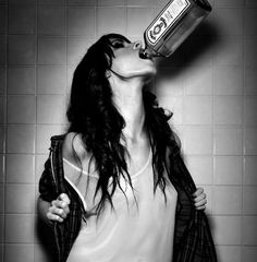 a woman drinking from a bottle while standing in front of a tiled wall