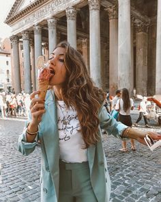 a woman eating an ice cream cone in front of a building with columns and people walking around