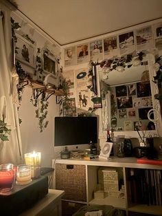 a desk with a computer monitor, candles and pictures on the wall in front of it