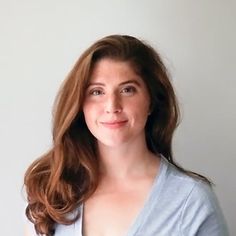 a woman with long brown hair wearing a blue shirt and smiling at the camera while standing in front of a white wall