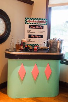 a green counter with pink diamond cutouts on it in front of a clock and window