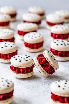 small macaroons decorated with red roses and white frosting are sitting on a table