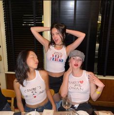 three women sitting at a table with plates and wine glasses in front of their faces