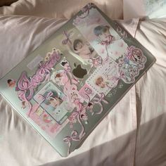 an open laptop computer sitting on top of a white bed covered in pink and silver stickers