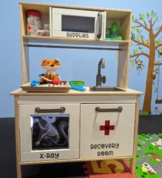 a toy kitchen with sink, stove and cupboards on the floor in front of a blue wall