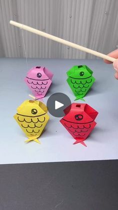 someone is holding chopsticks over some colorful origami fish shapes on a table