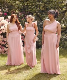 three bridesmaids in pink dresses standing on the grass and smiling at each other