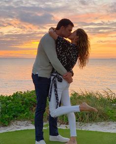 a man and woman kissing in front of the ocean at sunset with their arms around each other