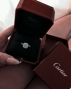 a woman's hand holding an engagement ring in a box