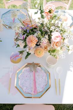 the table is set with pink and blue plates, silverware, flowers and napkins