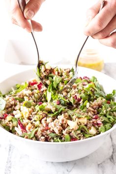 two hands holding spoons over a bowl filled with rice and vegetables on a marble table