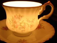 an antique tea cup and saucer with flowers on it, lit by a lamp