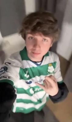 a young man in a green and white striped shirt pointing to the side with his finger