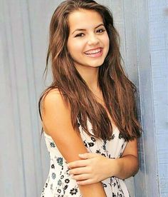 a young woman leaning against a blue wall with her arms crossed and smiling at the camera