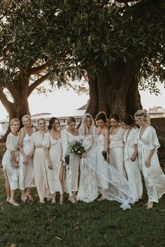 a group of women in white dresses standing next to each other under a large tree