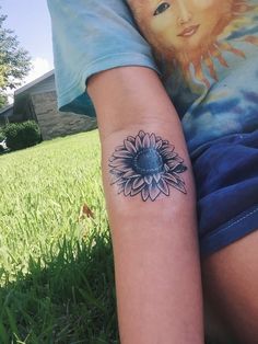 a person with a sunflower tattoo on their arm sitting in the grass next to a house